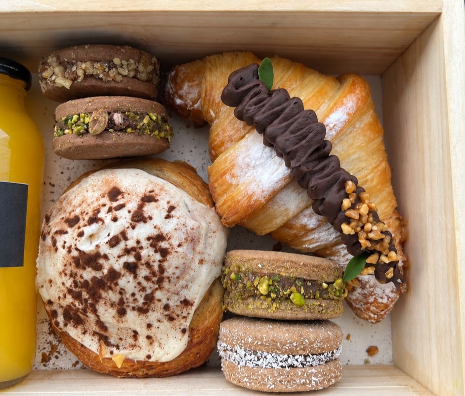 Caja de madera con croissant bañado, alfajores de pistacho y jugo